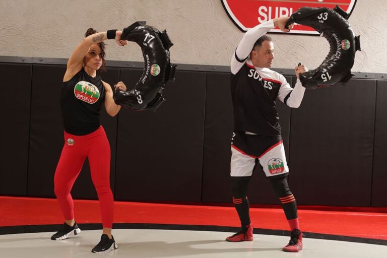 A man and a woman engaging in a Bulgarian bag workout.