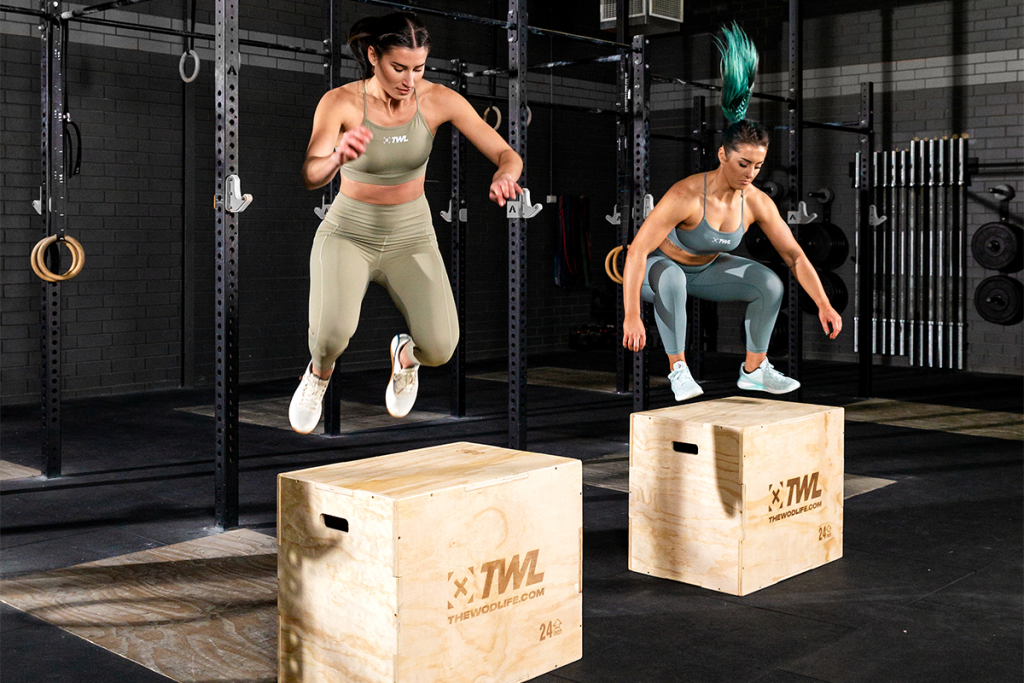 Two female athletes using two jump boxes at a gym.