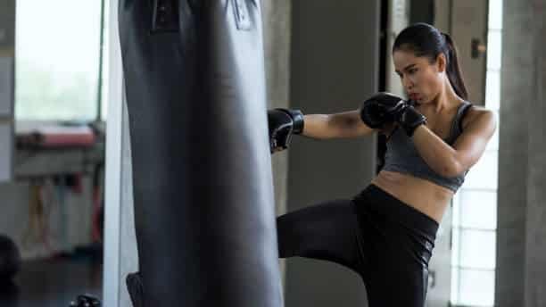 A woman kicking a punching bag wearing lace up boxing gloves